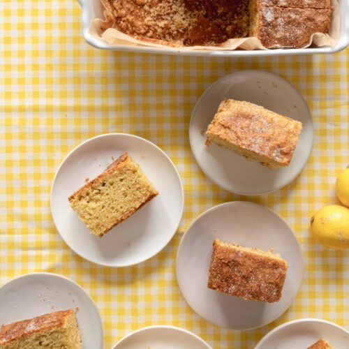 Las rebanadas de pastel se sirven en platos pequeños, rodeando una fuente para hornear con más pastel. La mesa está cubierta con un mantel de cuadros amarillos y blancos. En la esquina también se ven tres limones.