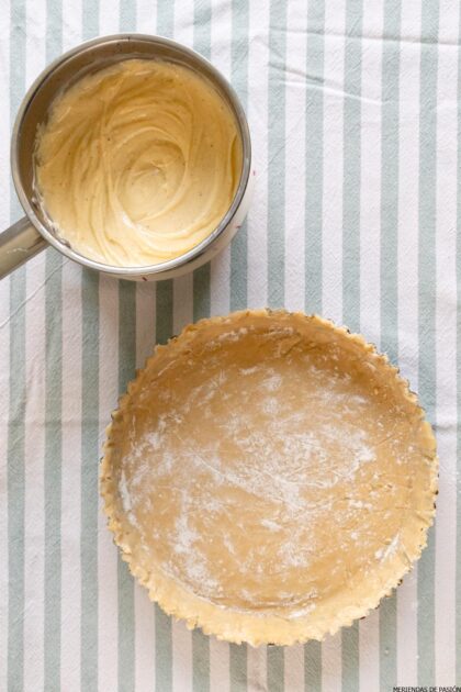 Se prepara una masa de tarta en un molde para tarta estriado, junto a una olla que contiene un relleno cremoso, todo sobre una superficie de tela rayada.