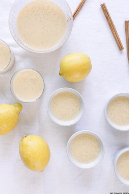 Platos variados de arroz con leche con limones, ramas de canela y un gran tazón de arroz con leche sobre un mantel blanco.