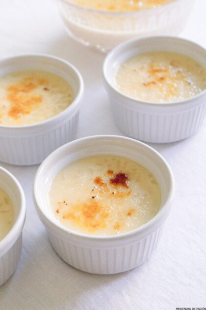 Cuatro moldes de cerámica blanca llenos de arroz con leche, con una capa de azúcar caramelizada, están dispuestos sobre una superficie blanca.